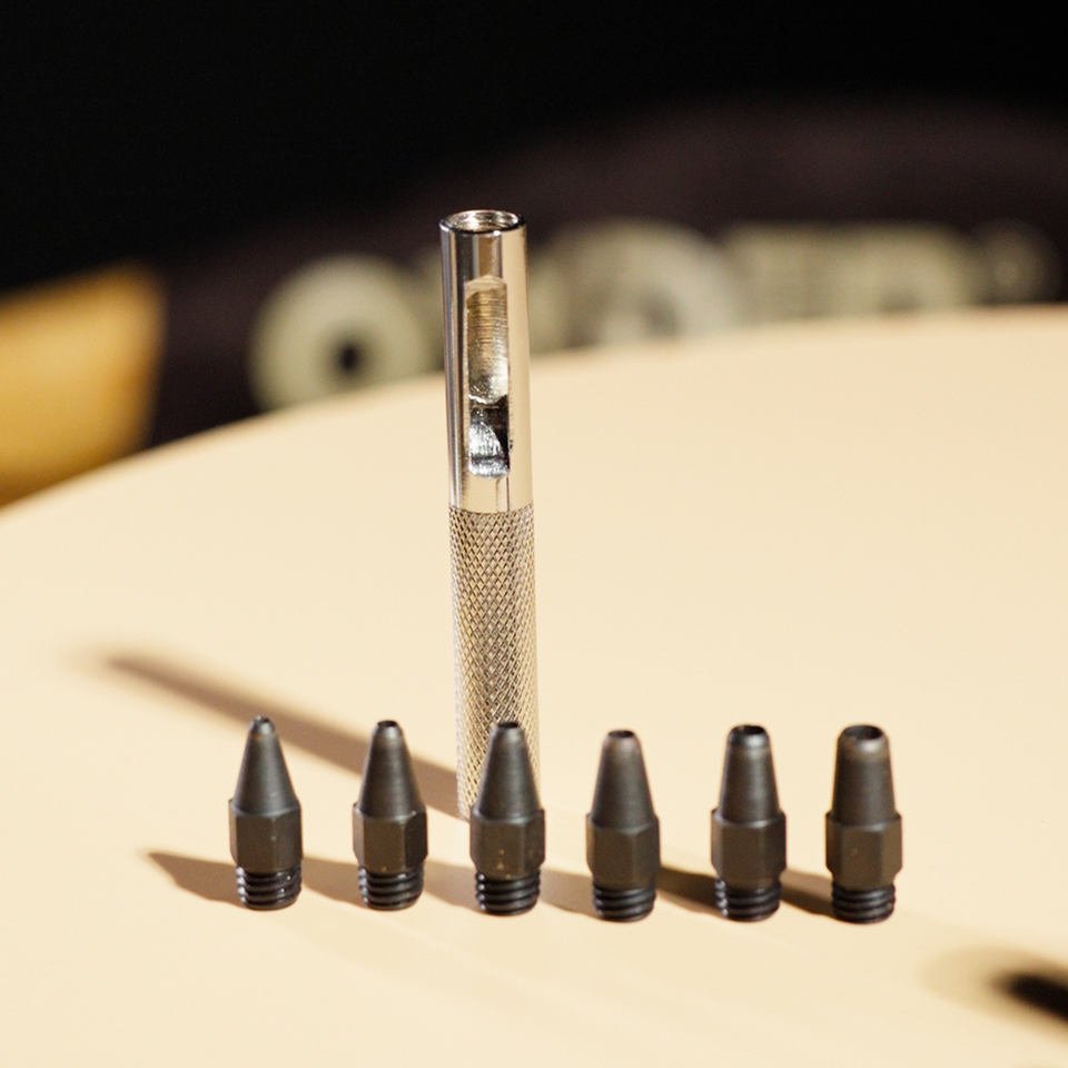 Knurled hollow leather punch handle standing behind six threaded hollow cutting tips